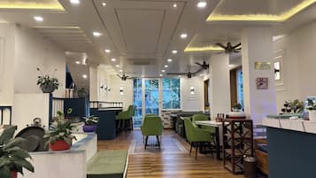 Un interior de restaurante con una barra larga, sillas verdes y plantas en macetas.