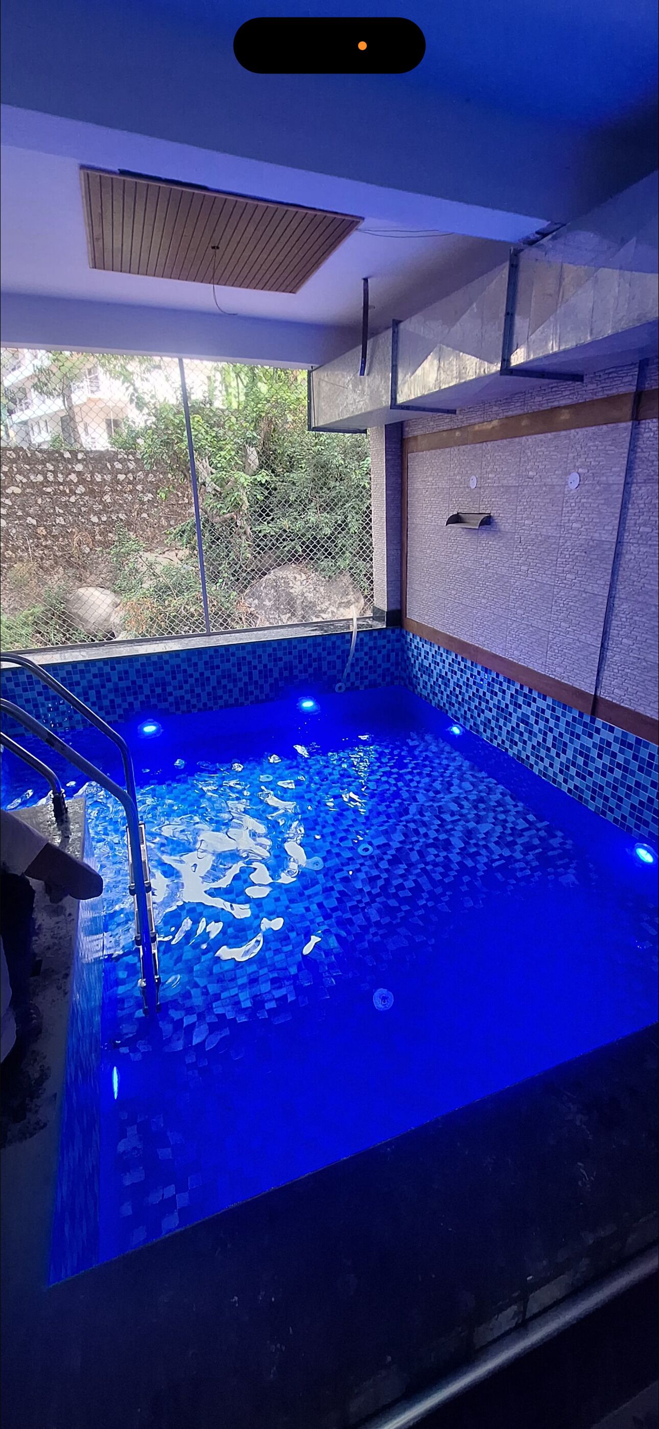 Una piscina con iluminación azul en su interior, rodeada por una valla y un muro de piedra.