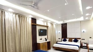 A hotel room with a large bed, a smaller bed, a TV, a wardrobe, and a ceiling fan.