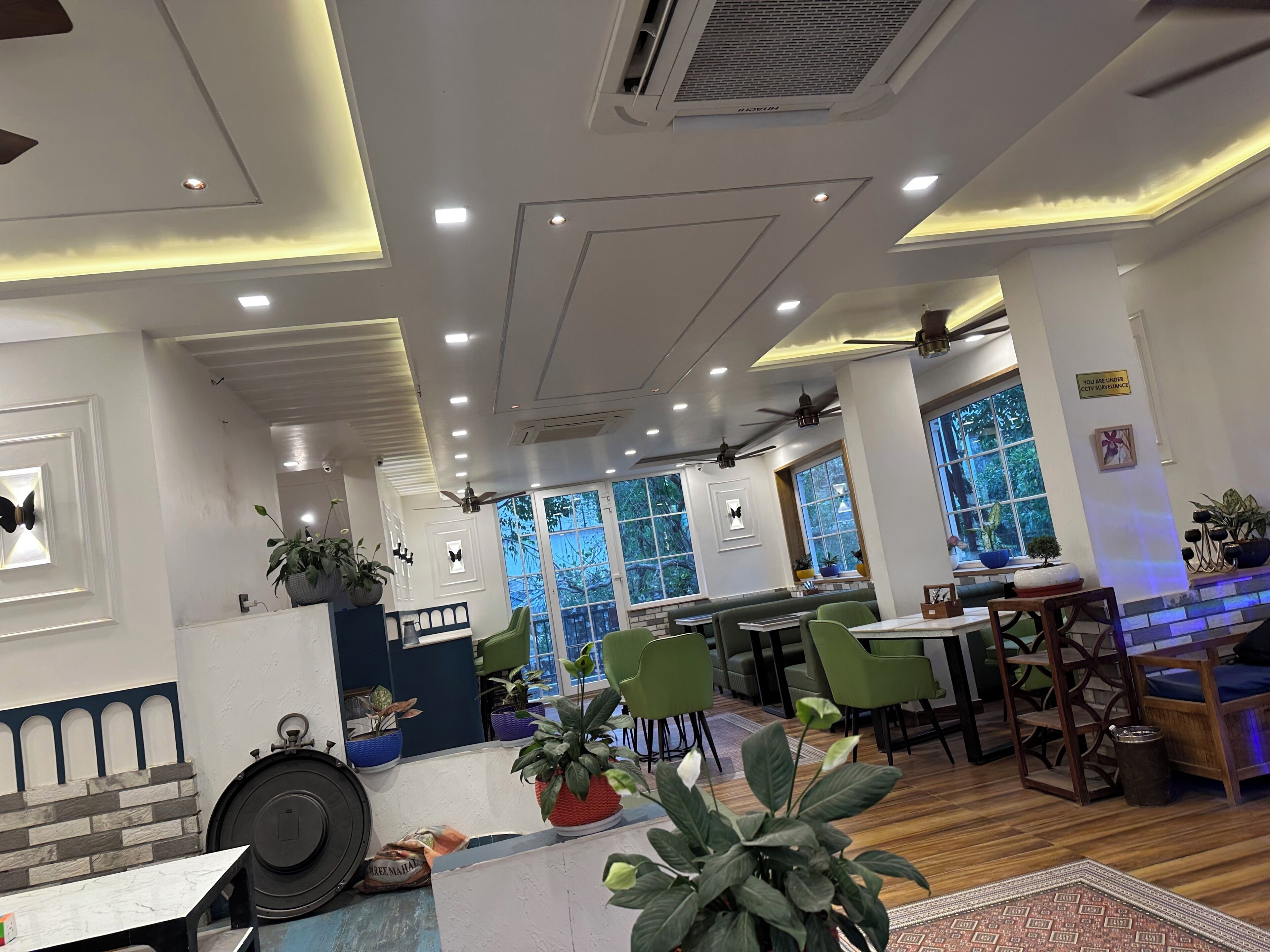 Ein Restaurantinneres mit verschiedenen Sitzbereichen, Deckenventilatoren und Topfpflanzen.