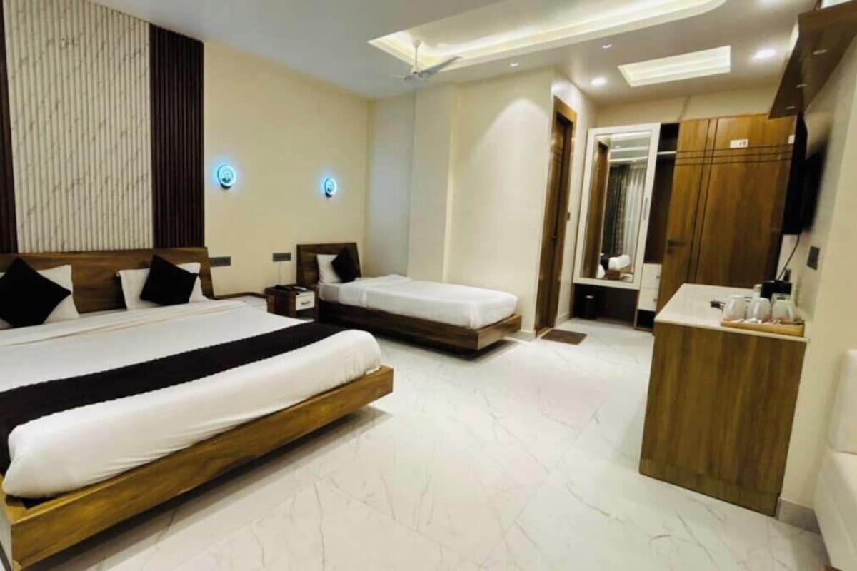 A hotel room with two beds, a wooden wardrobe, a vanity with a mirror, and a ceiling light.