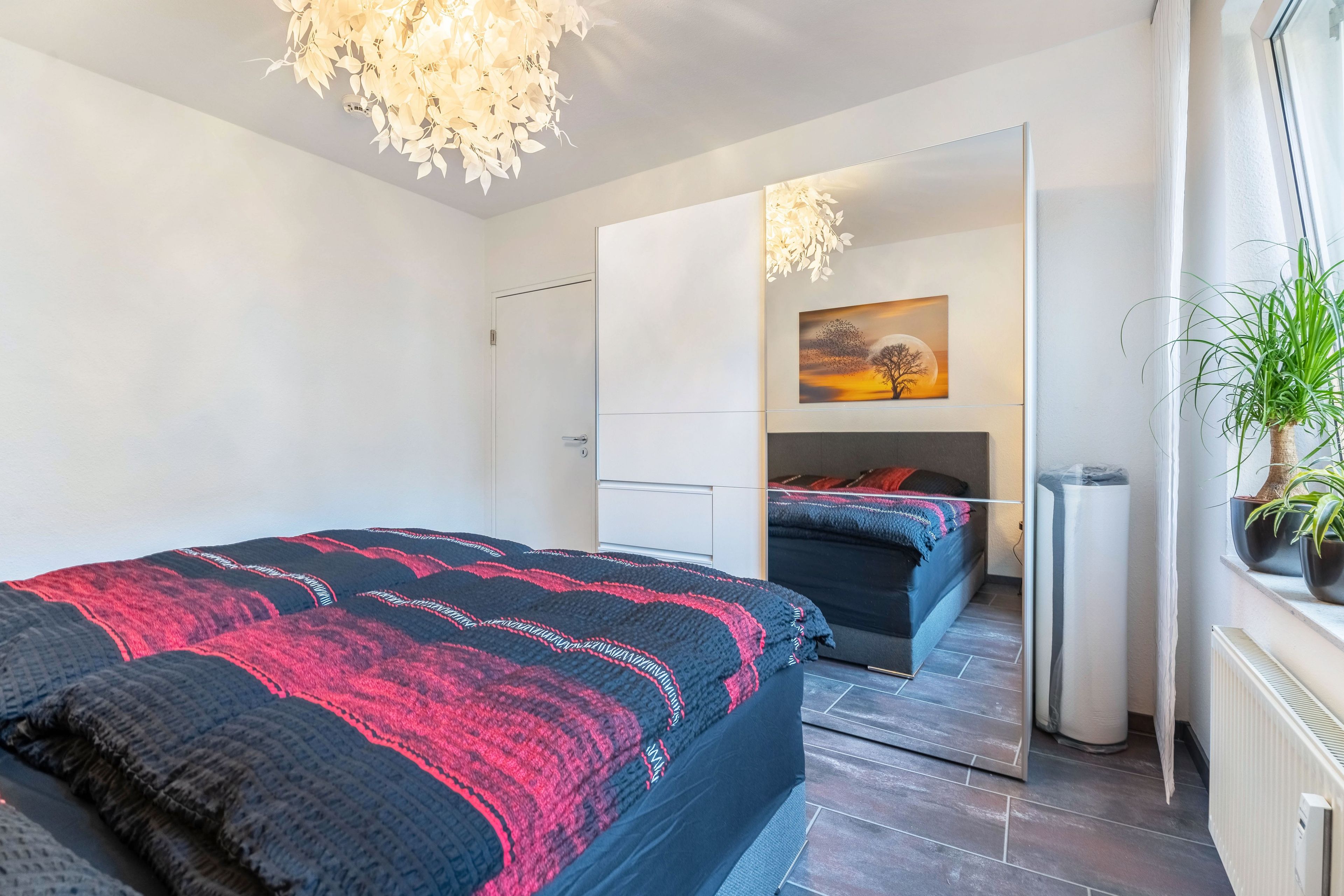Quarto moderno com cama grande, mesa de cabeceira, espelho e janela com vista para o exterior.
