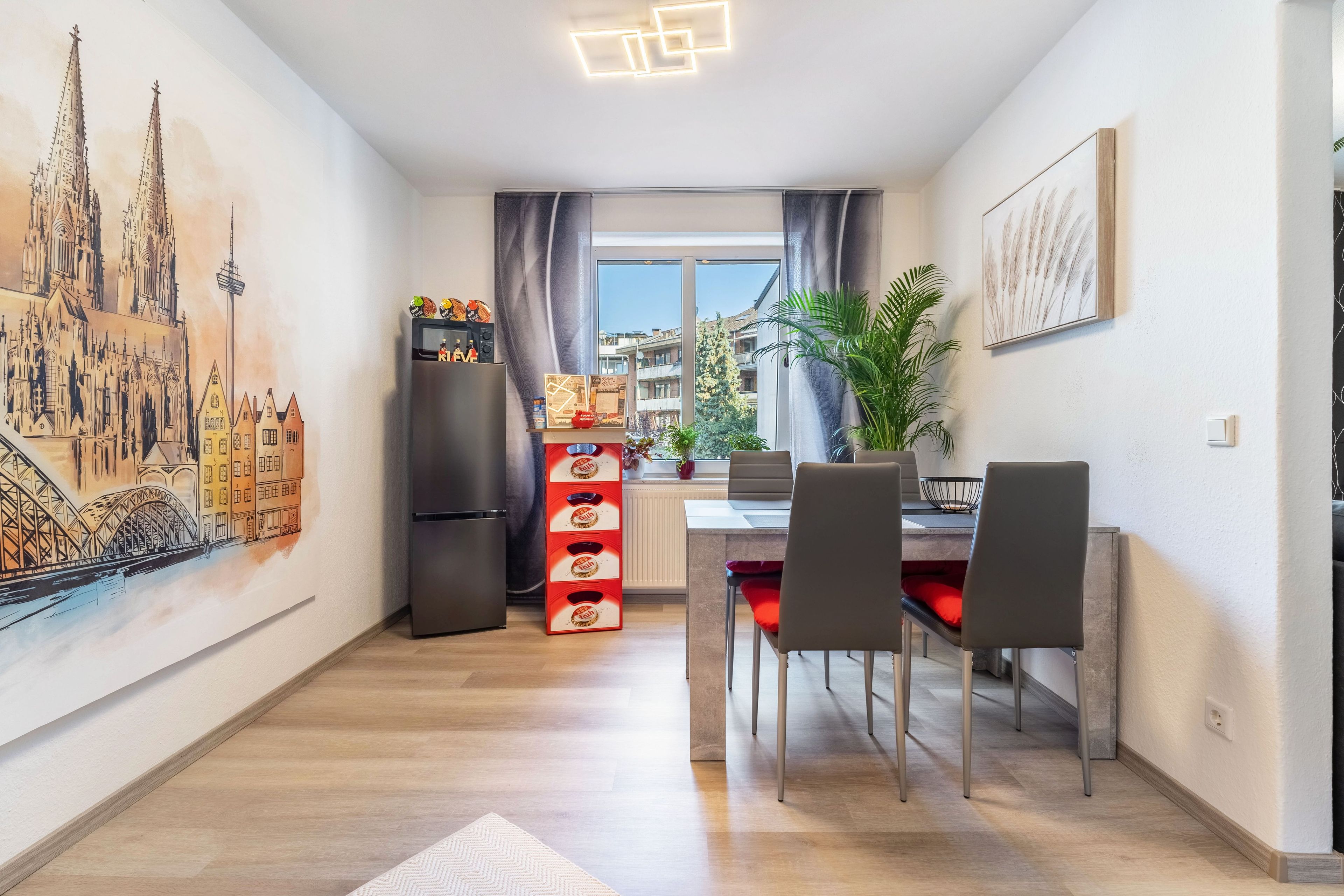 A modern kitchen with a dining area, a refrigerator, and a window with a view of buildings.
