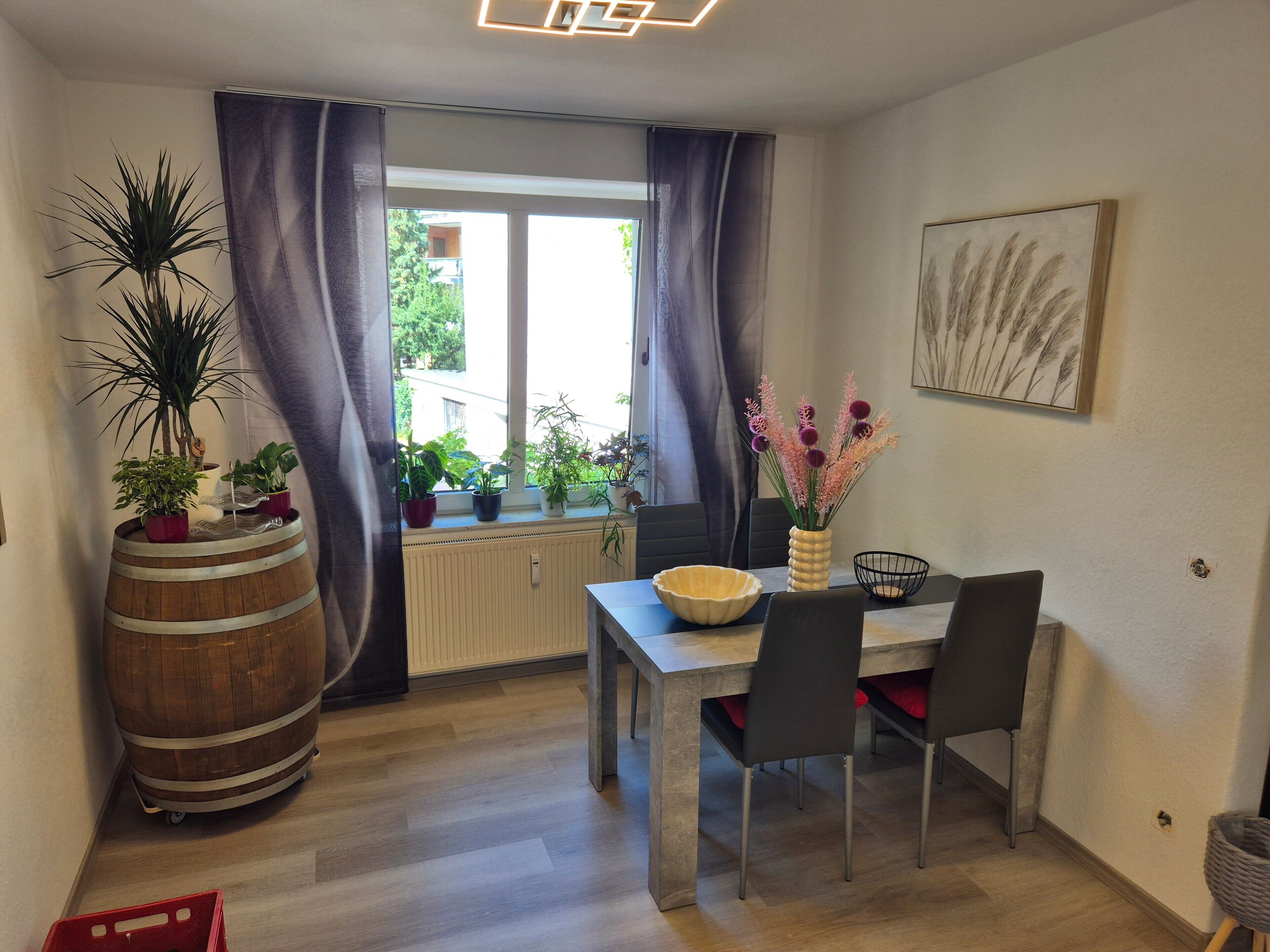 Un coin repas avec une table en bois, des chaises, une plante en pot, un vase avec des fleurs et une fenêtre avec des rideaux.