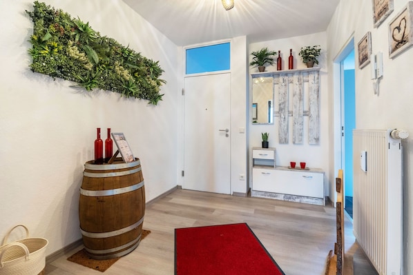 Un pasillo con un barril de madera, un tapete rojo y un arreglo de plantas en la pared.