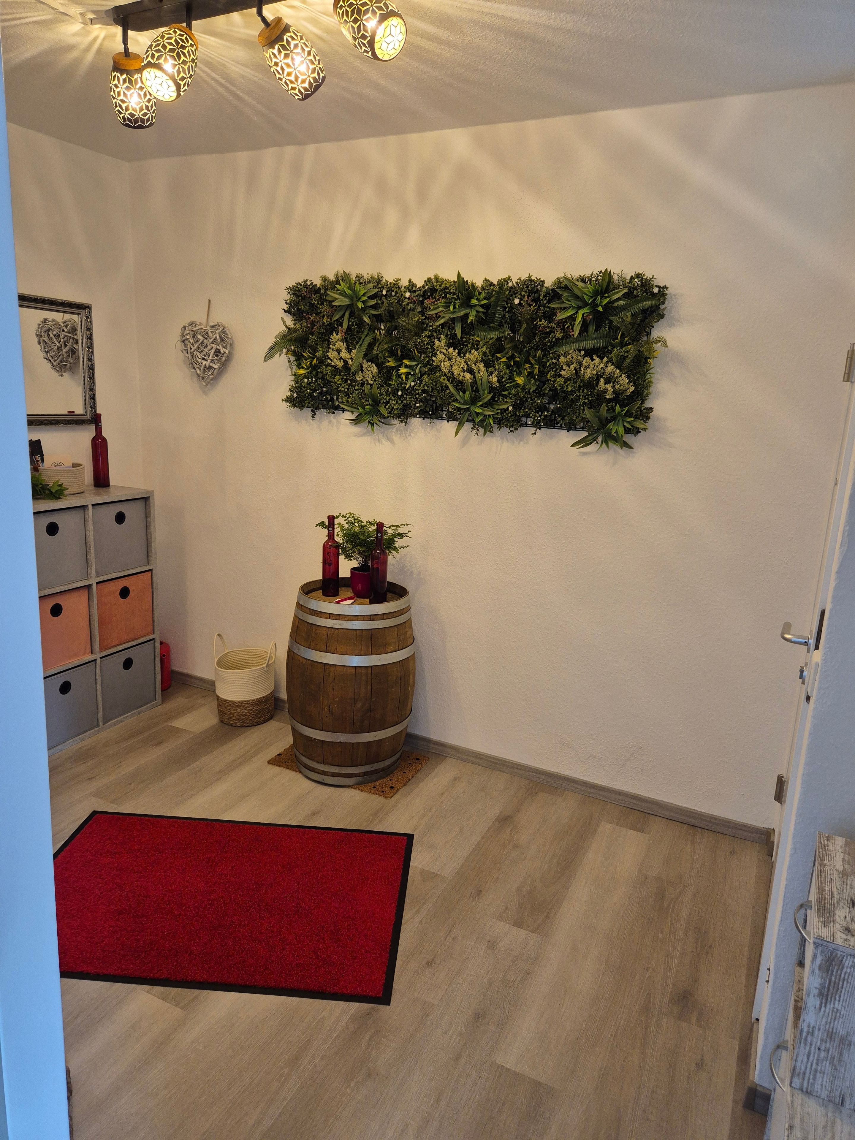 A room with a wooden barrel, a red rug, a wall-mounted plant, and a mirror with a heart-shaped decoration.