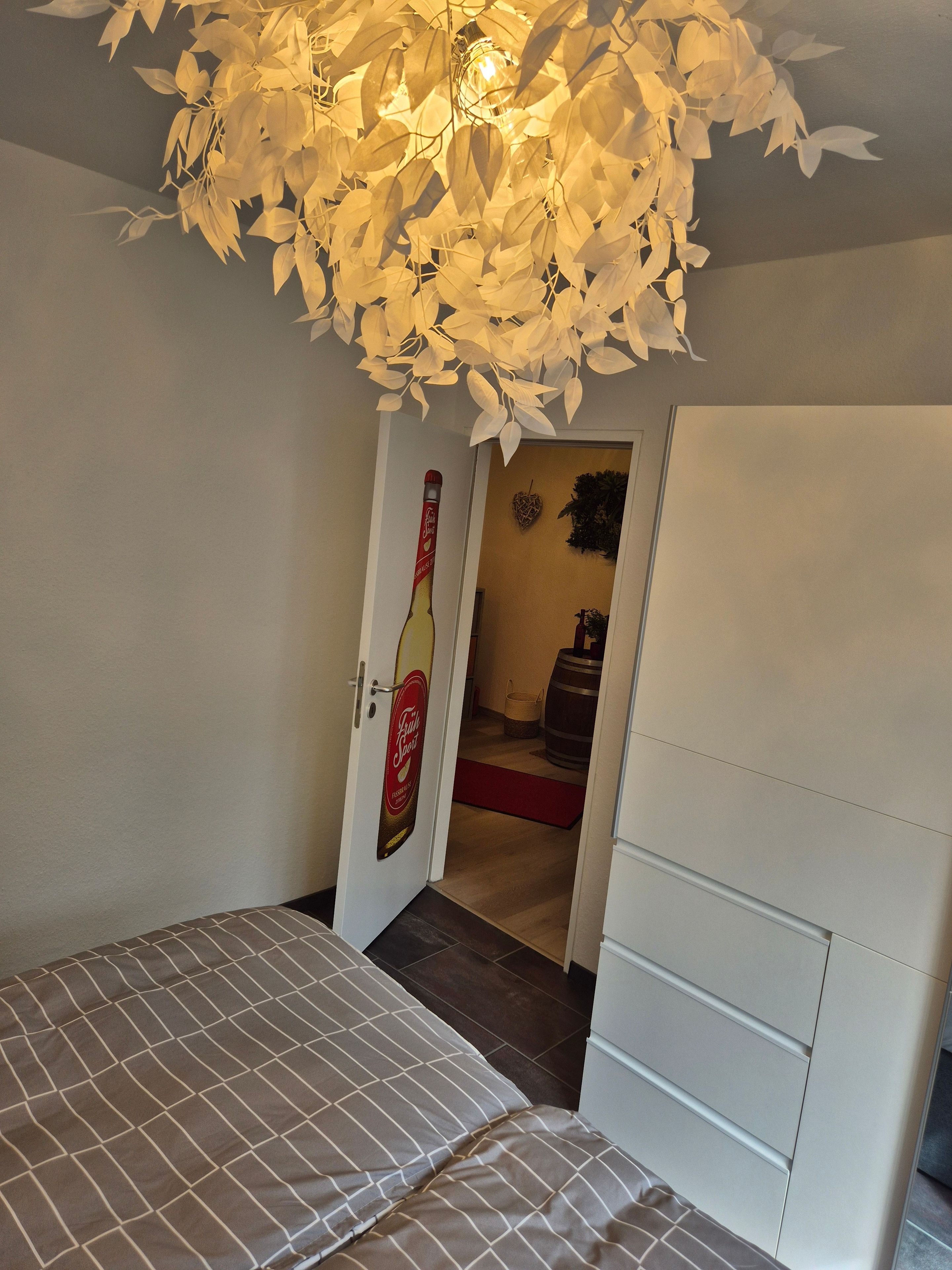 A bedroom with a bed, a wardrobe, a door with a beer bottle decal, and a ceiling light fixture.