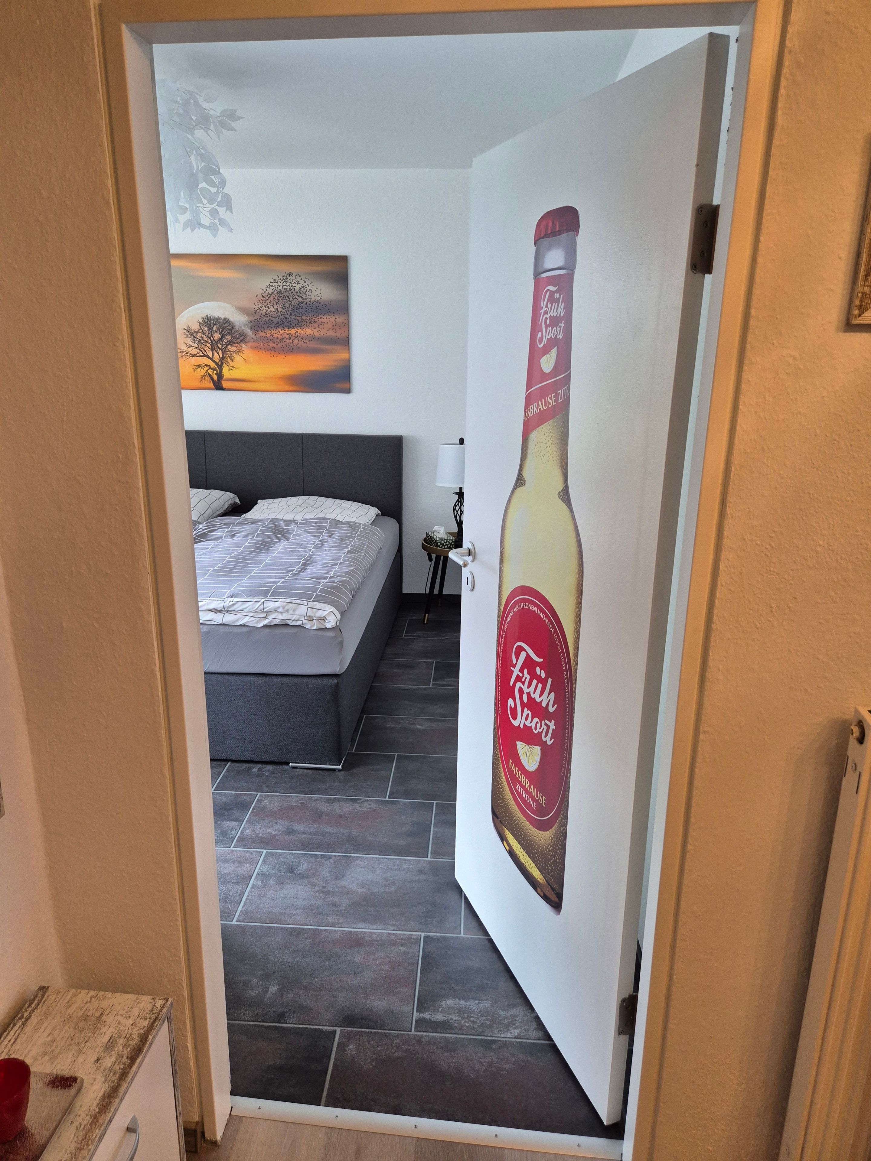 Een slaapkamer met een bed, nachtkastje, lamp en een schilderij aan de muur.