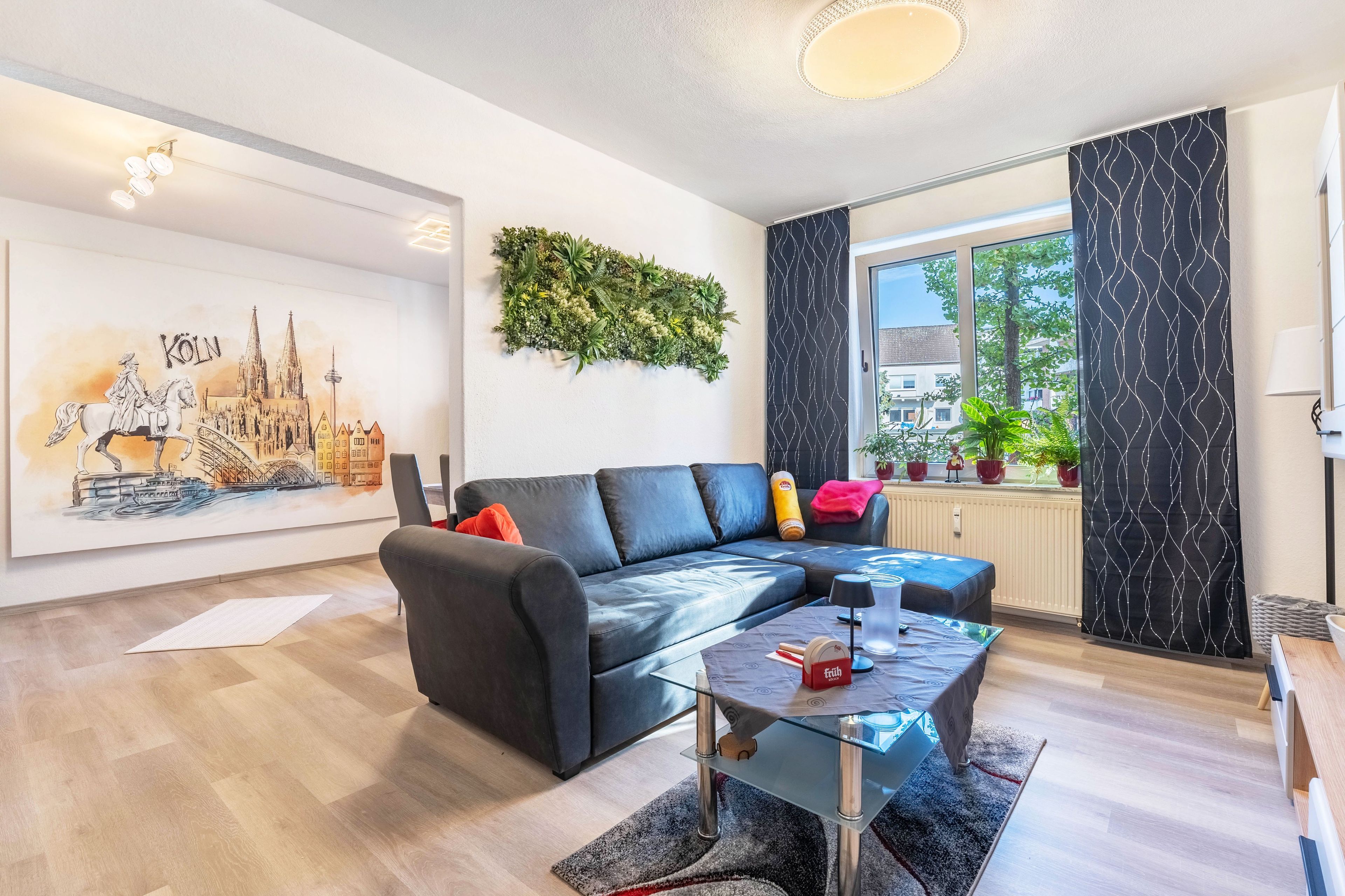 A modern living room with a black leather sofa, a glass coffee table, and a cityscape painting on the wall.