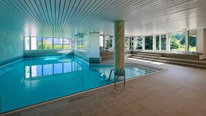 An indoor swimming pool with clear glass walls, a tiled floor, and a ceiling with a linear pattern. - Holiday apartment in Laax with swimming pool (Laax)