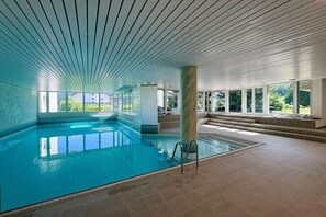 An indoor swimming pool with clear glass walls, a tiled floor, and a ceiling with a linear pattern. - Holiday apartment in Laax with swimming pool (Laax)