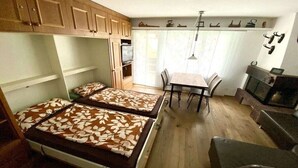 A compact room with two beds, a dining table, chairs, a fireplace, and wooden cabinets. - Holiday apartment in Laax with swimming pool (Laax)