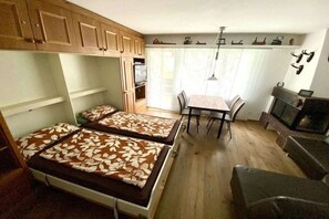 A compact room with two beds, a dining table, chairs, a fireplace, and wooden cabinets. - Holiday apartment in Laax with swimming pool (Laax)