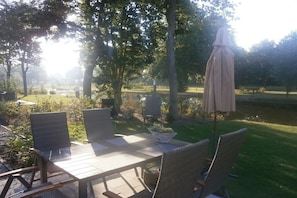 An outdoor patio with a table and chairs, surrounded by trees and a body of water. - Holiday home with 2 bedrooms (RB Hulshorst)