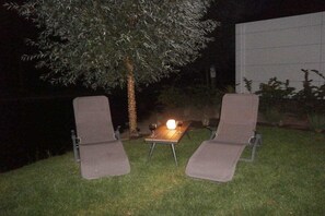Two outdoor lounge chairs with a table and a candle between them, set on a grassy area at night. - Holiday home with 2 bedrooms (RB Hulshorst)