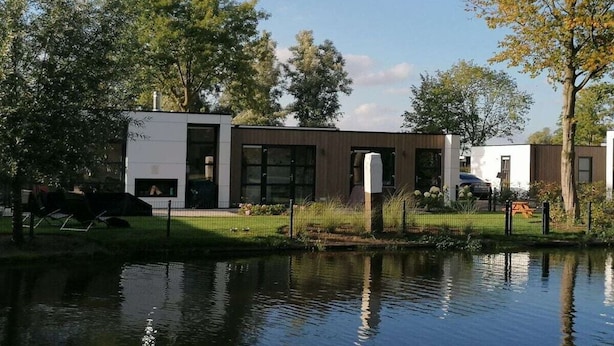 A modern building with a reflective water body in front, surrounded by trees and a grassy area. - Holiday home with 2 bedrooms (RB Hulshorst)