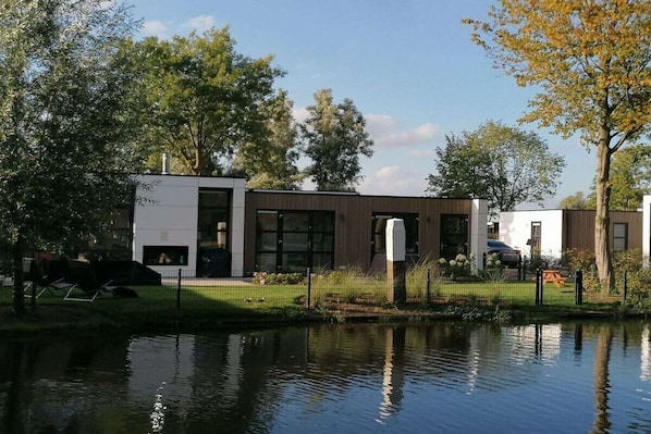 A modern building with a reflective water body in front, surrounded by trees and a grassy area. - Holiday home with 2 bedrooms (RB Hulshorst)
