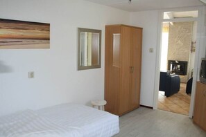 Een slaapkamer met een bed, een kledingkast, een klein krukje en een schilderij aan de muur.