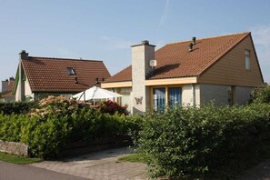 A two-story house with a brick roof, a chimney, and a small garden area with a pathway leading to the entrance. - Holiday home with 3 bedrooms (Julianadorp aan Zee)