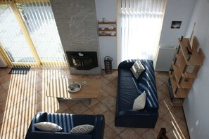 A living room with a fireplace, a sofa, a coffee table, and a view through large windows. - Holiday home with 3 bedrooms (Julianadorp aan Zee)
