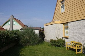 A residential property with a well-maintained lawn, a wooden bench, and a white brick house with a yellow trim. - Holiday home with 3 bedrooms (Julianadorp aan Zee)