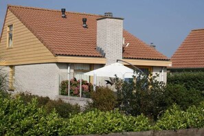 Una casa amb teulada inclinada, una xemeneia i un para-sol blanc.