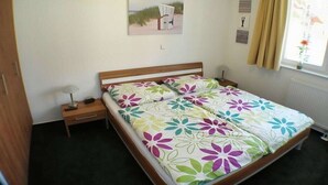 Un dormitorio con cama, mesita de noche, lámpara, ventana con cortinas y un cuadro en la pared.