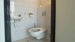 Un bagno piccolo e pulito con un water, un lavandino e un portasciugamani per carta igienica.