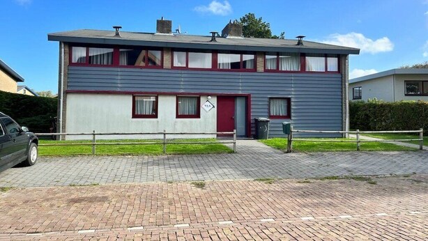 Un edificio a due piani con una porta rossa e finestre, un vialetto lastricato e un'auto parcheggiata.