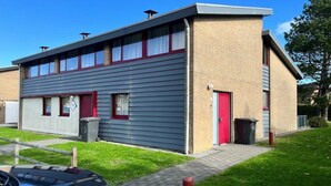 Un edificio a due piani con una porta rossa e finestre con tende bianche.