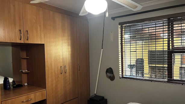 Un dormitorio con cama, armario de madera, escritorio y ventilador de techo.