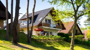 Ein zweistöckiges Haus mit geneigtem Dach und einem Balkon, mit einem roten Sonnenschirm.