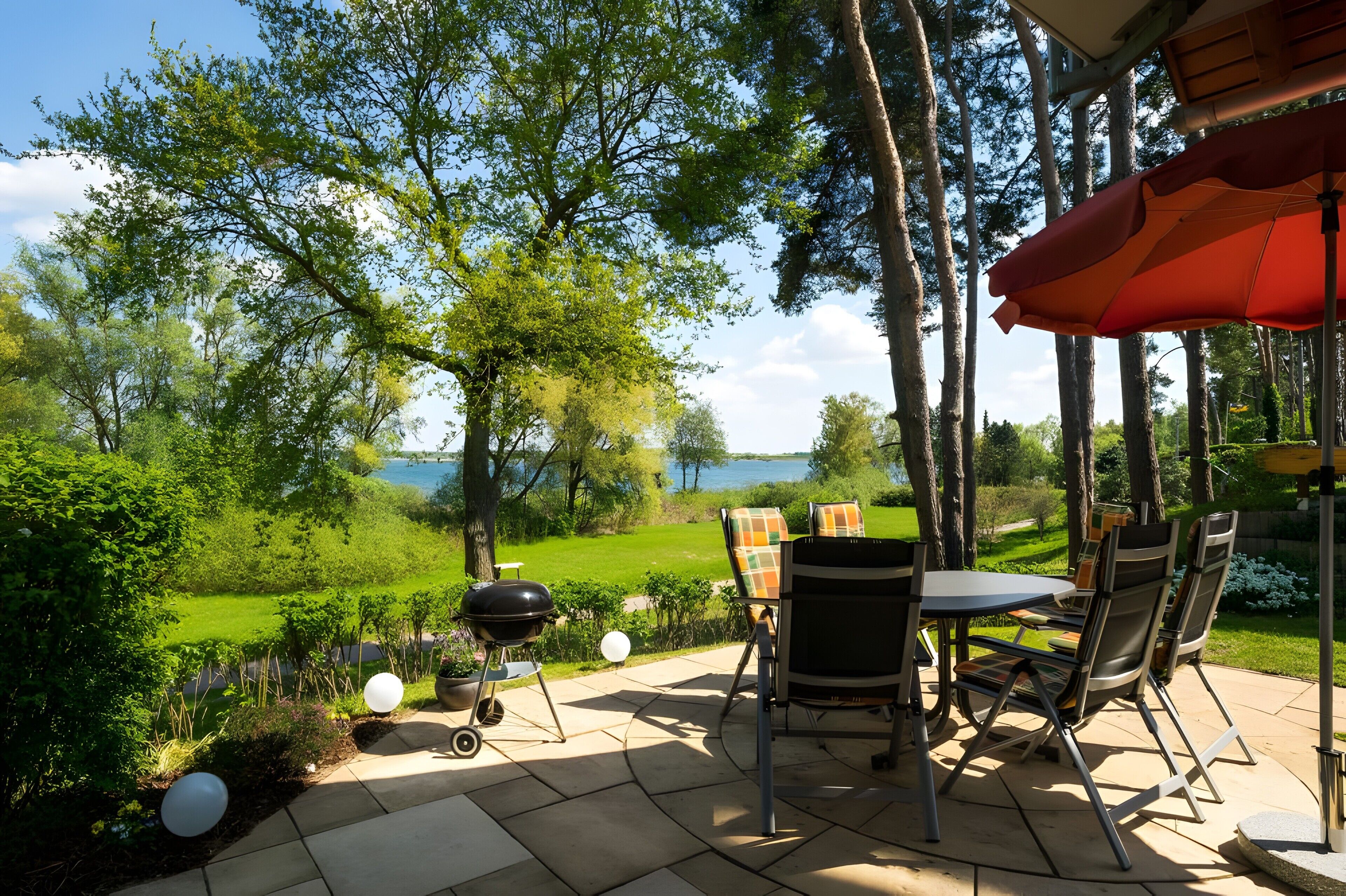 Eine Terrasse im Freien mit Tisch, Stühlen, einem Grill und Blick auf einen See.