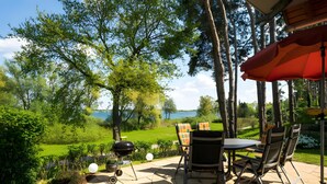 Eine Terrasse im Freien mit Tisch, Stühlen, einem Grill und Blick auf einen See.