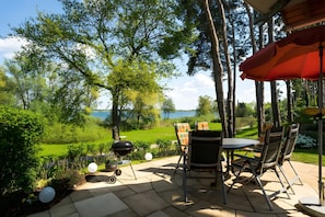 An outdoor patio with a table and chairs, a grill, and a view of a lake. - Apartment 'Haus 3 Eg' with Sea View, Private Terrace and Wi-Fi (Röbel)