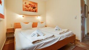 Ein Doppelbett mit weißen Leinen und Handtüchern, ein Holz-Kopfteil, ein Blumenbild und ein Lichtschalter an der Wand.