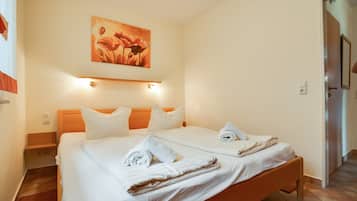 Ein Doppelbett mit weißen Leinen und Handtüchern, ein Holz-Kopfteil, ein Blumenbild und ein Lichtschalter an der Wand.