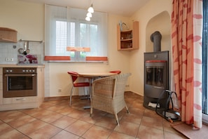 A kitchen with a stove, oven, dining table with chairs, a window with curtains, and a wood-burning stove. - Apartment 'Haus 3 EG & UG' with Lake View, Private Terrace and Wi-Fi (Röbel)