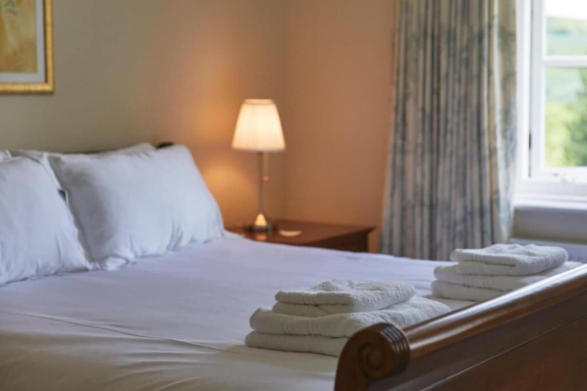 A neatly made bed with white linens and a stack of folded towels on the headboard.