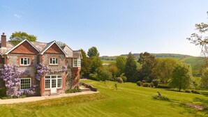 A large house with a well-maintained lawn and a view of rolling hills in the distance. - Lordington Park (Chichester)
