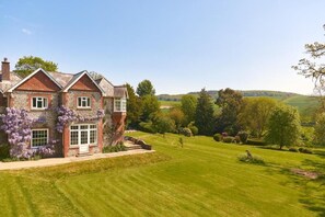 A large house with a well-maintained lawn and a view of rolling hills in the distance. - Lordington Park (Chichester)