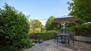An outdoor patio area with stone flooring, a table with chairs, and a large umbrella. - Lordington Park (Chichester)