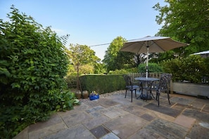An outdoor patio area with stone flooring, a table with chairs, and a large umbrella. - Lordington Park (Chichester)