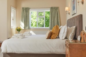 A neatly made bed with pillows, a bedside table with a lamp, and a window with curtains. - Lordington Park (Chichester)