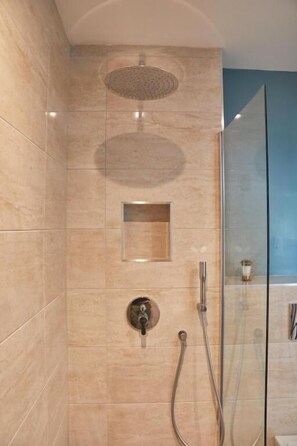 A modern bathroom with a glass shower enclosure, a handheld showerhead, and a wall-mounted faucet. - Lordington Park (Chichester)