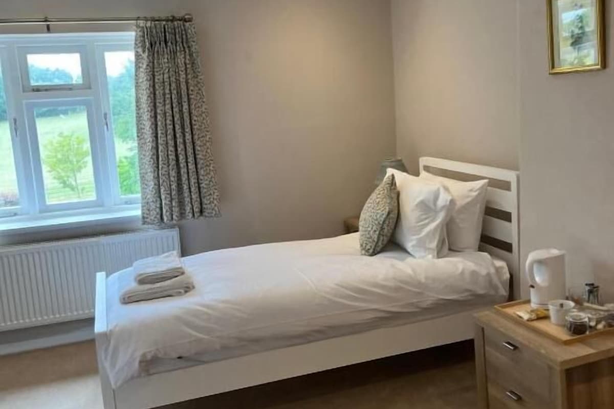 A bedroom with a bed, bedside table, and a window with curtains.
