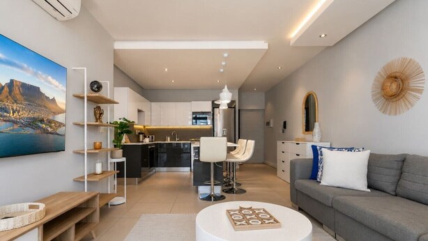 Una sala de estar moderna con un sofá gris, una mesa de centro redonda y un televisor montado en la pared.