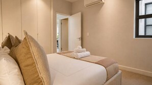 Un dormitorio con cama, almohadas, una ventana y un equipo de aire acondicionado.