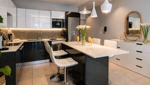 Una cocina moderna con una isla central, taburetes de bar, iluminación colgante y un espejo grande.