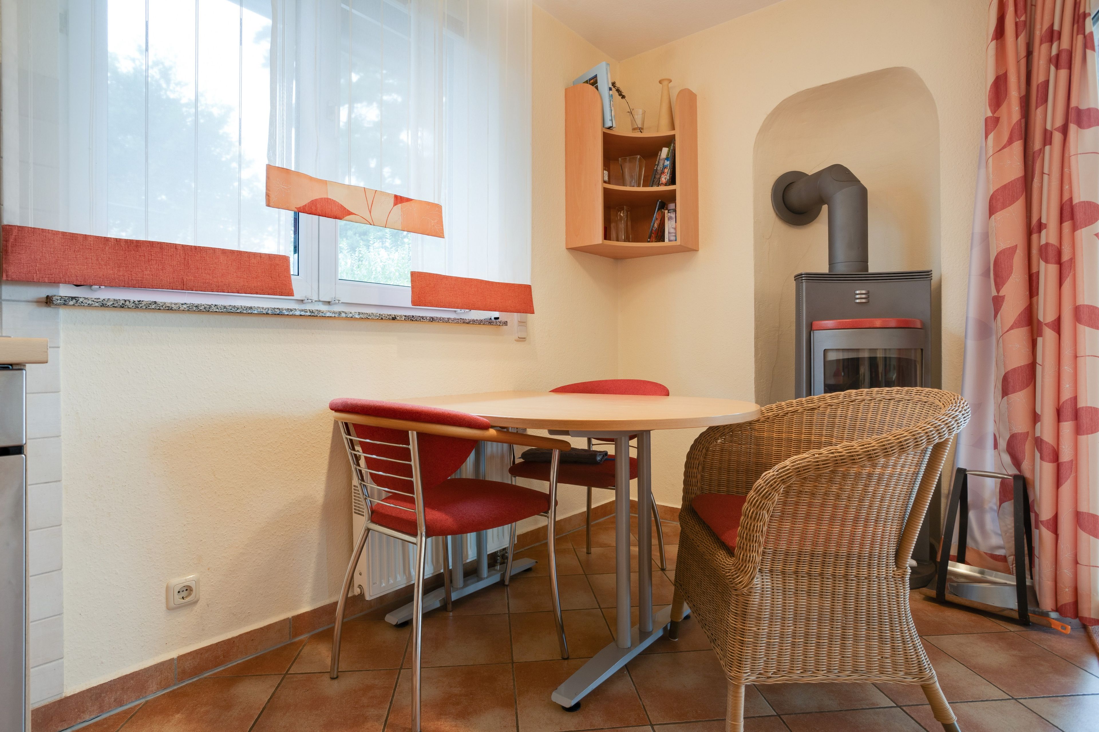 Una cocina pequeña con una mesa, sillas, una estantería empotrada y un estufa de leña.
